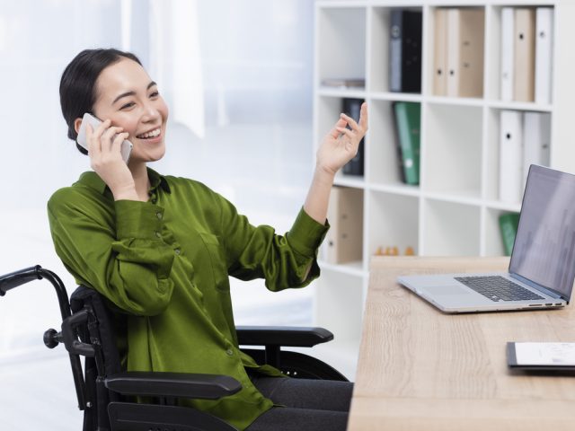 mujer en silla de ruedas frente a un escritorio hablando por el móvil